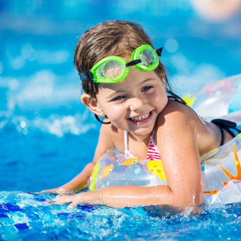 A little girl with goggles enjoys playing in a bright blue PeakPools pool on a sunny day